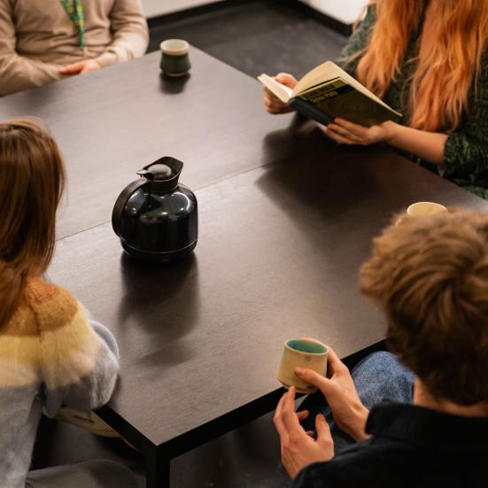Gruppe af mennesker samlet om et bord med bog og kaffe