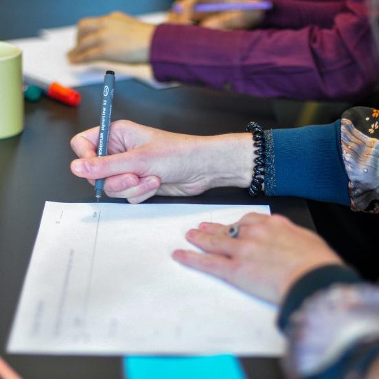 foto af bord med udsnit af mennesker, der skriver på papir. omgivet af glas og krus