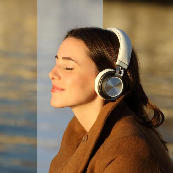 Portræt i profil af en kvinde med store hovedtelefoner og lukkede øjne i varmt sollys ved vandet.