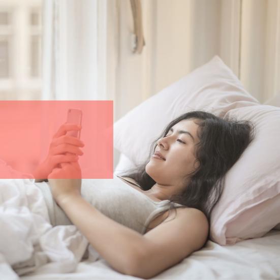 Ung kvinde ligger i seng og læser på sin telefon