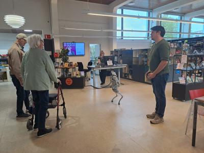 Mads fra ITK står sammen med robotten Bob i biblioteksrummet. To ældre mennesker kigger interesseret på robotten. 