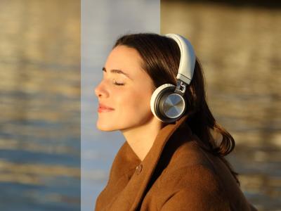 Portræt i profil af en kvinde med store hovedtelefoner og lukkede øjne i varmt sollys ved vandet.