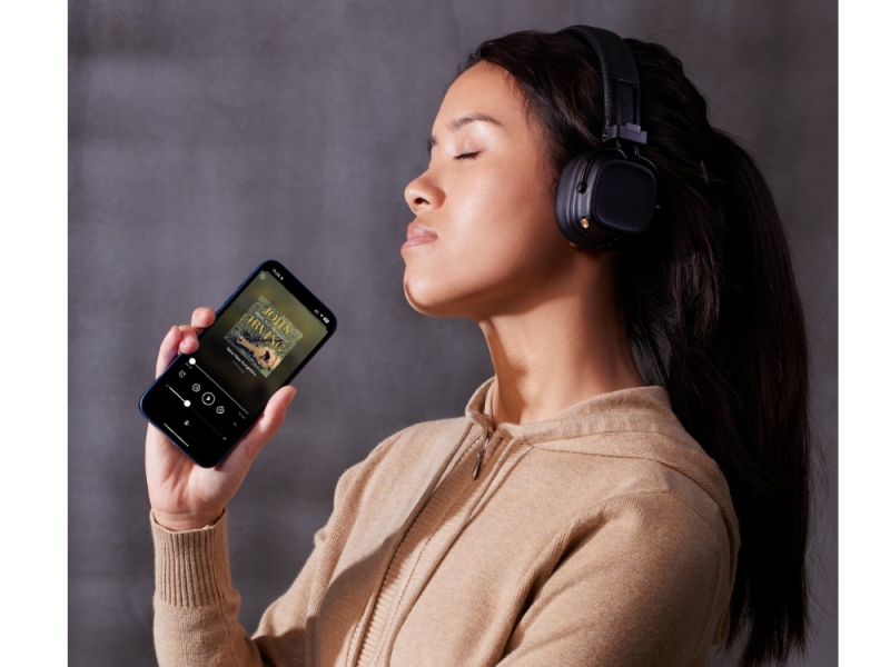 Kvinde der står med en smartphone og har høretelefoner på. Hun lytter til en lydbog.