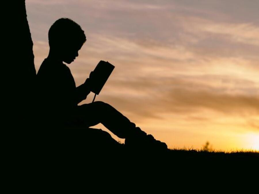 En dreng der læser i solnedgangens skær