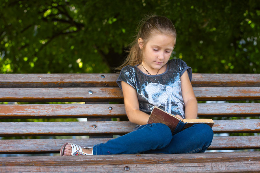 Pige sidder på en bænk og læser i en bog