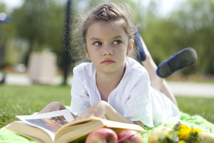 Pige der ligger i græsset og læser i en bog