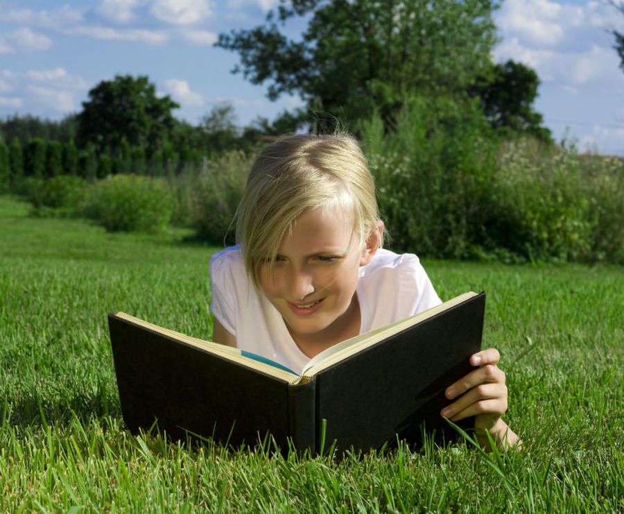 En pige ligger på græsset og læser en bog