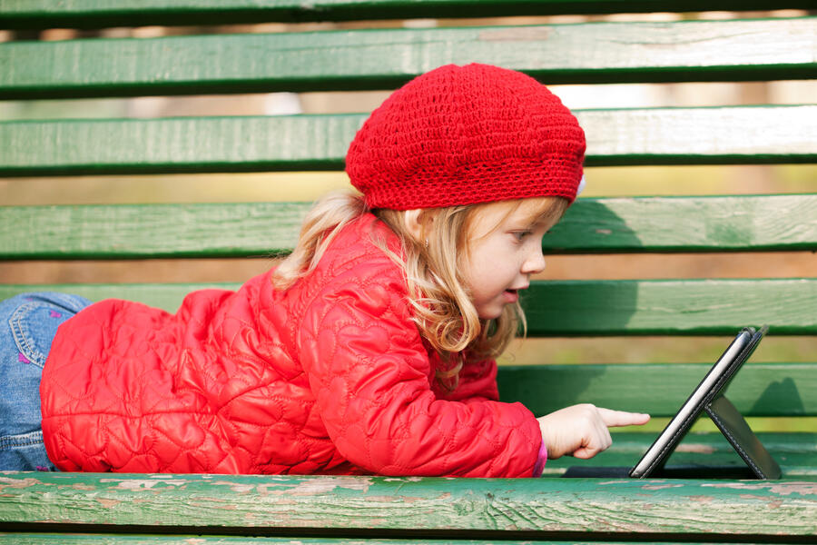Pige der ligger på en bænk og læser i en e-bog