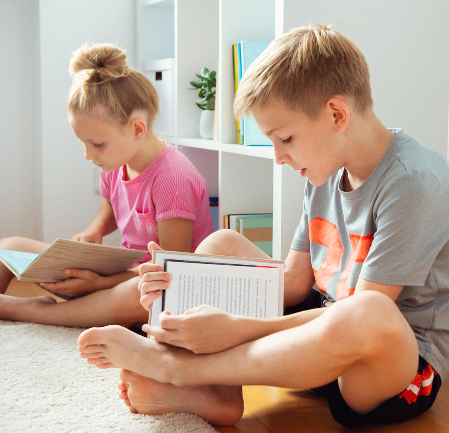2 børn der sidder på gulvet og læser i bøger