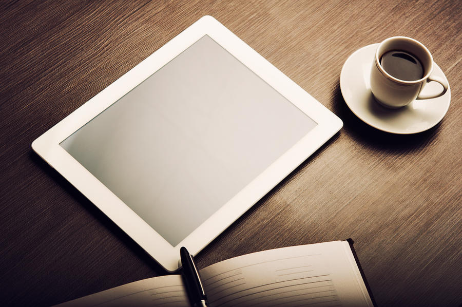 En tablet og en kop kaffe på et bord
