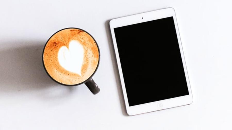 En tablet og en kop kaffe på et bord