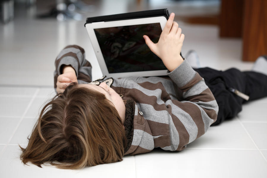 Barn ligger på gulvet og læser på en tablet
