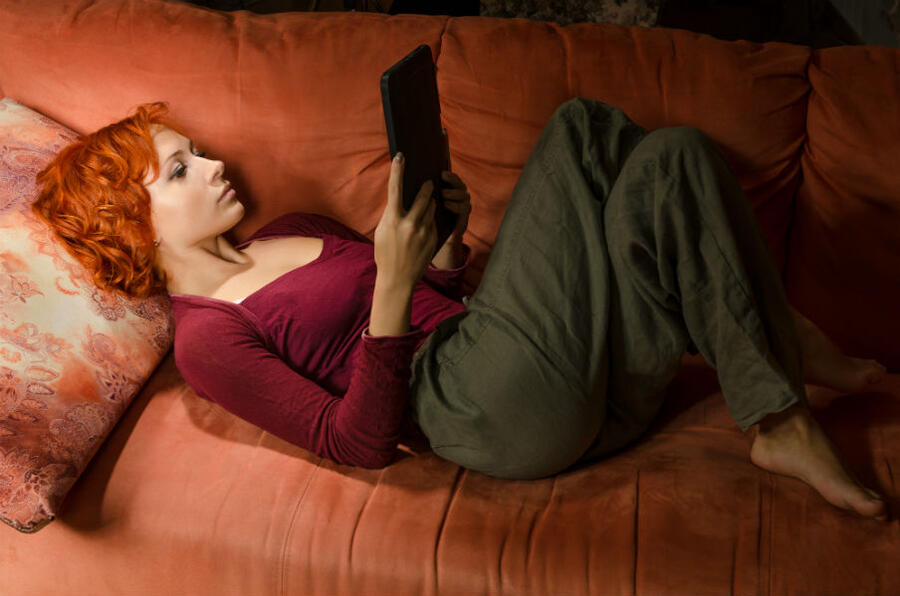 Kvinde der ligger i en sofa og læser en e-bog