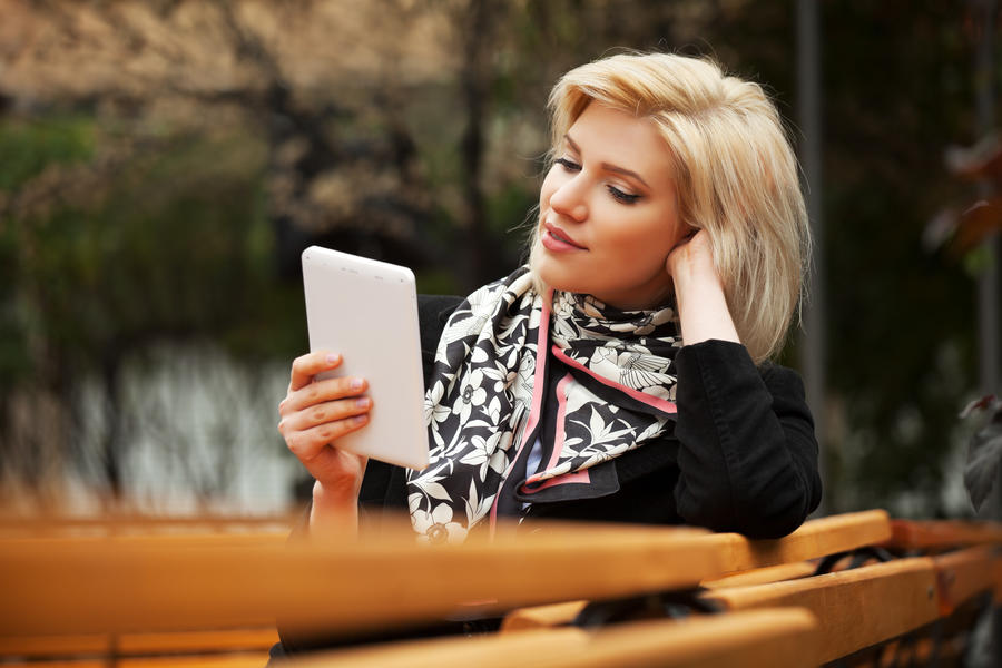 En kvinde sidder på en bænk og læser på en tablet