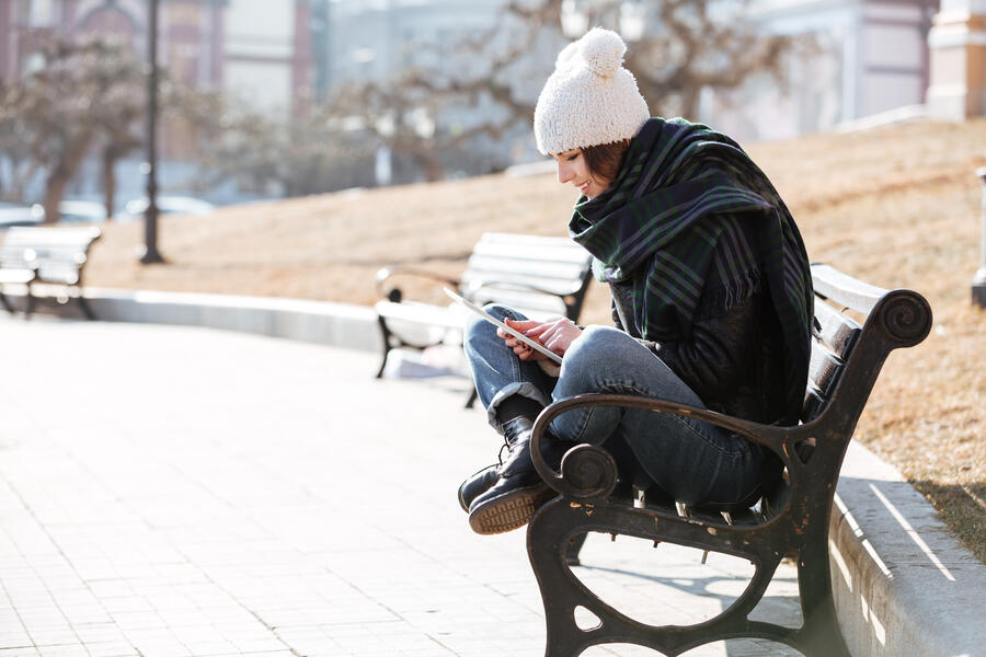 Kvinde der sidder på en bænk og læser en e-bog