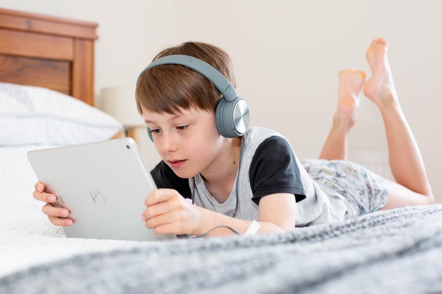 Dreng med høretelefoner, der ligger på en seng med en tablet