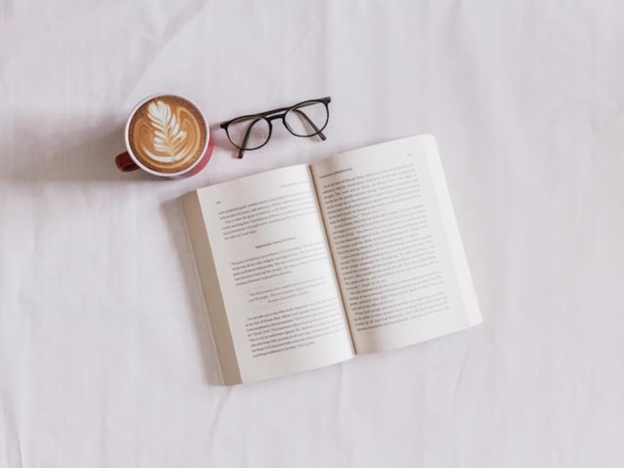 En bog, en kop kaffe og et par briller på et bord