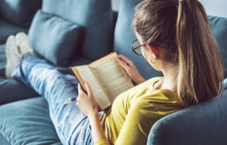 Kvinde der sidder i en sofa og læser i en bog