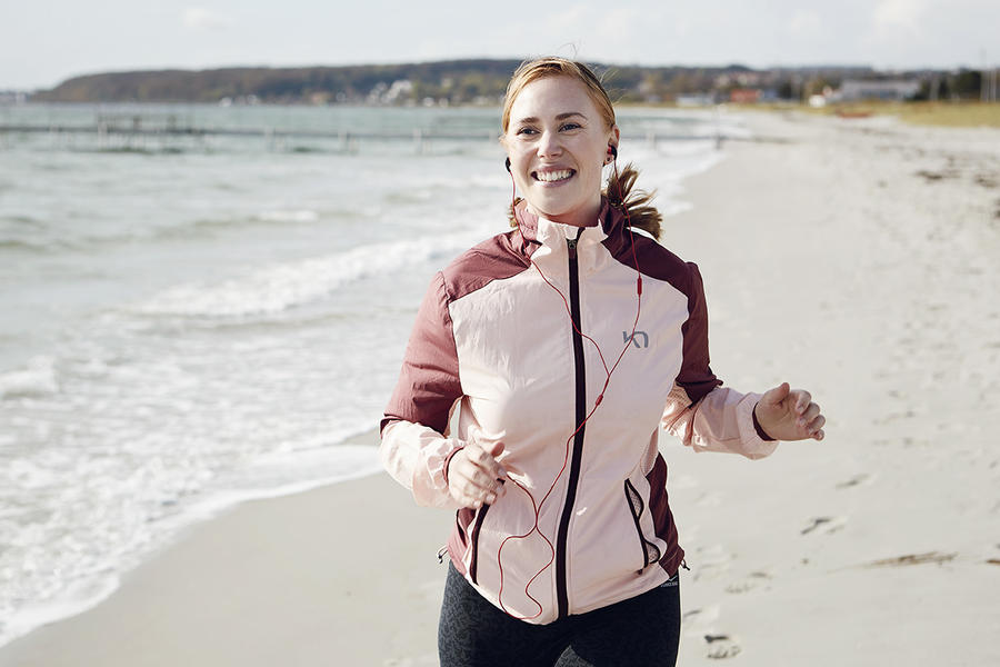 Kvinde løber på stranden og lytter til en lydbog
