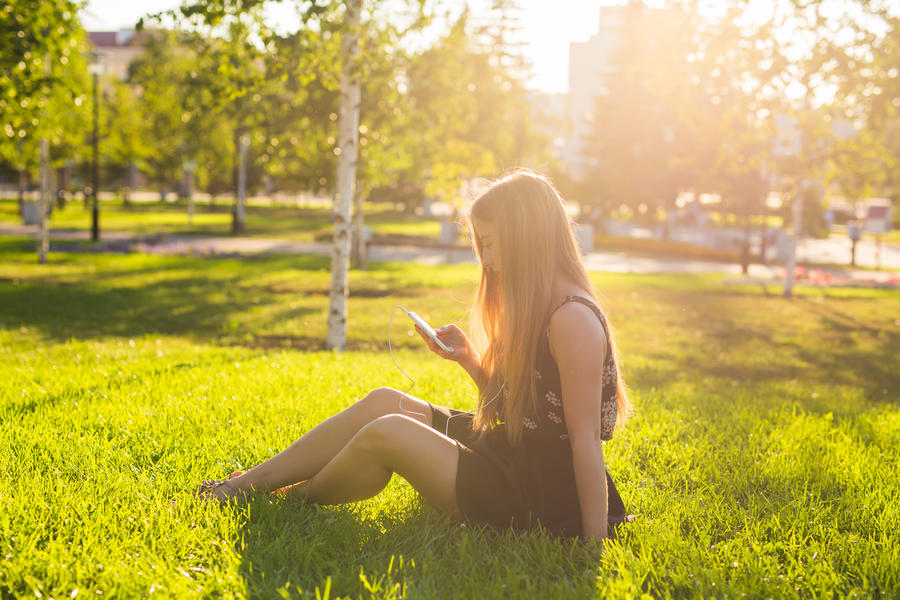 Kvinde der sidder i græsset og lytter til en lydbog