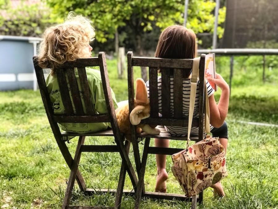To Børn sidder på stole på en græsplæne og læser