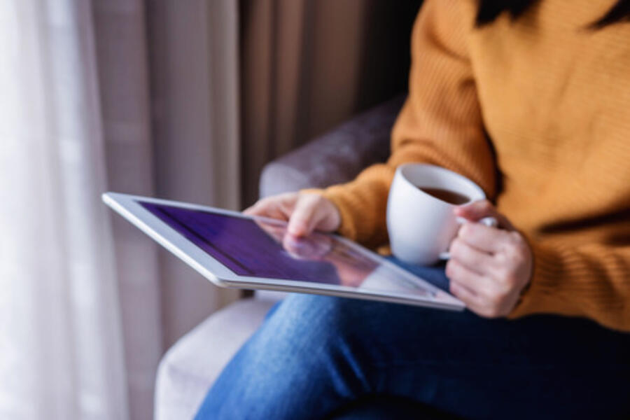 Udsnit af billede hvor du ser en tablet og en persons ben og arm der holder en kop kaffe