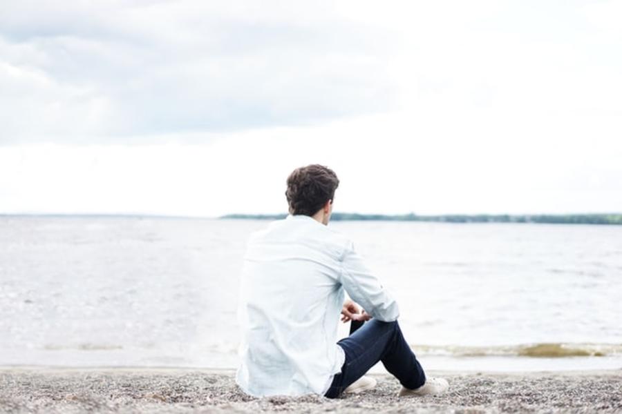 En mand sidder på stranden og ser ud over vandet