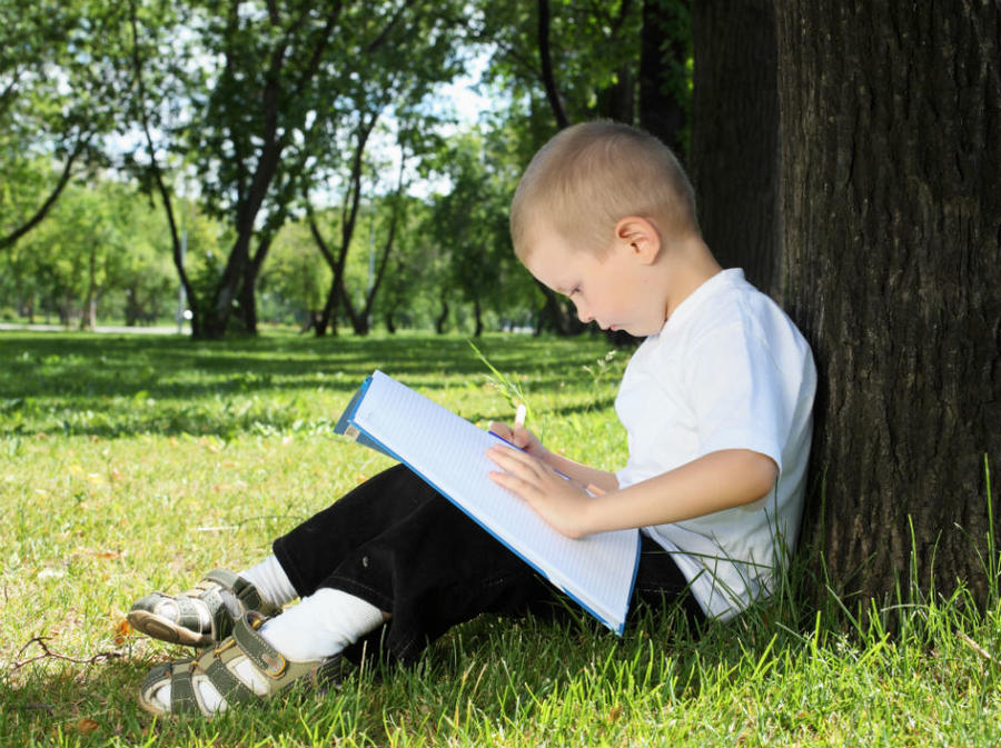 En dreng sidder på græsset og læser i en bog