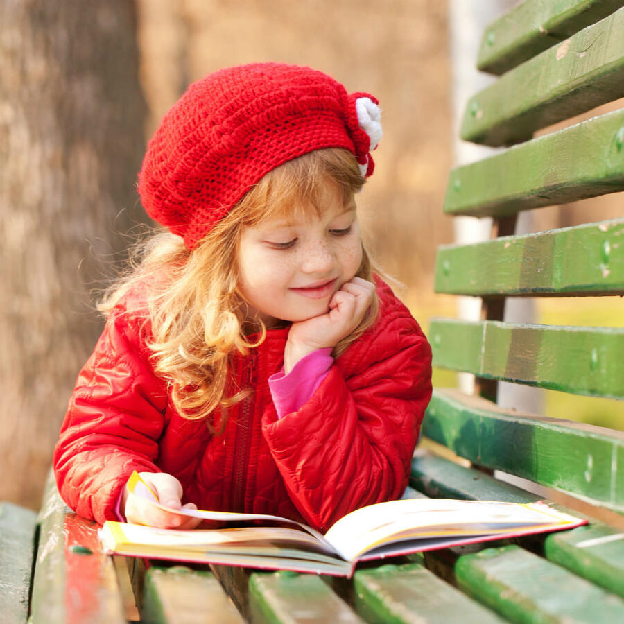 Pige der ligger på en bænk og læser en bog