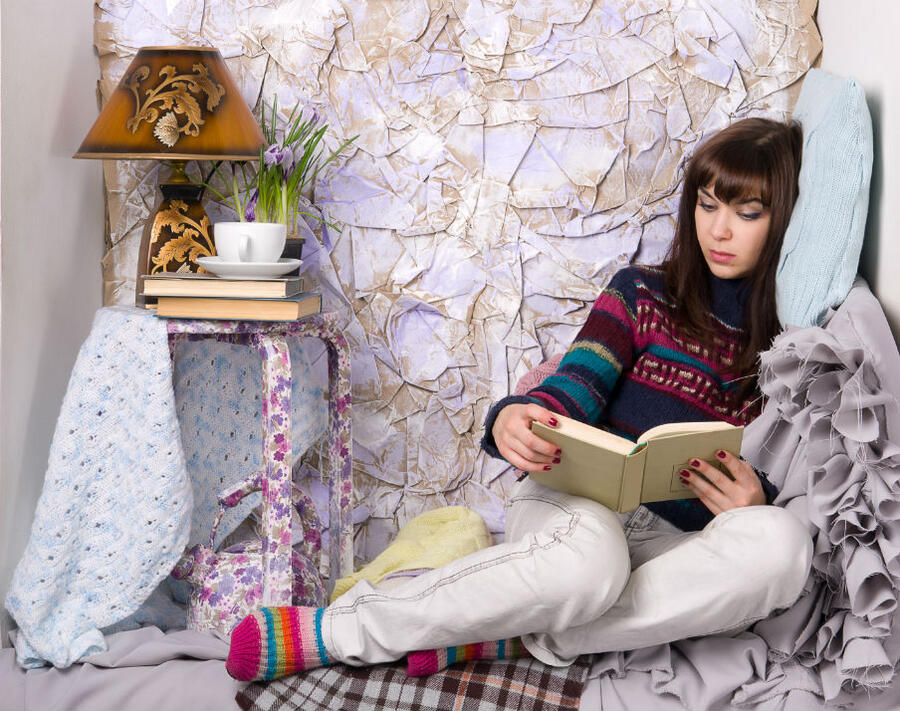 Ung pige sidder i en seng og læser en bog